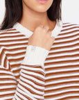 A person models The Upside's BOO KNIT JUMPER, a brown and white striped organic cotton sweater, showcasing its ribbed white cuffs and neckline while holding the collar against a plain white background.