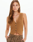 A woman with long brown hair models The Upside's BABYLON BUTTON KNIT VEST—a slim fit, sleeveless, buttoned brown knit waistcoat—paired with leopard print pants, standing hands-in-pockets against a plain white background.
