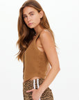 A young woman with long brown hair models The Upside's BABYLON BUTTON KNIT VEST, a slim fit sleeveless brown top, paired with leopard print pants with white stripes, posing in profile against a plain white background.