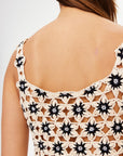A close-up of a person’s upper back shows them wearing The Upside's LUMINARY LILY CROCHET TOP, featuring a cream and black floral pattern. Their straight brown hair is partially visible.