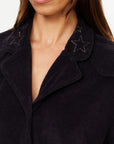 A woman models The Upside's SADDLE UP COLLARED HARDY SHIRT, a dark organic cotton piece with a textured finish and star embroidery on the collar, shown from the shoulders up.
