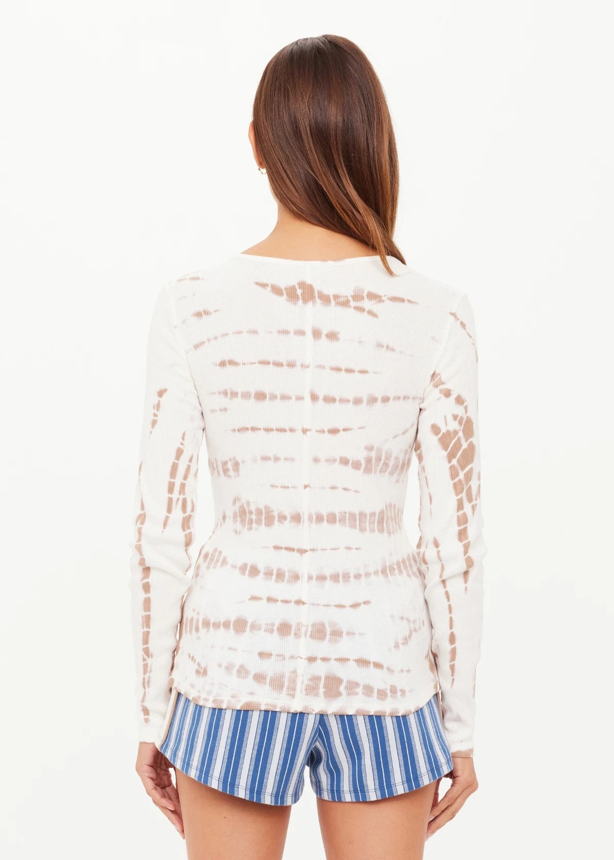 A person with straight brown hair wears The Upside AYLA CHRISSY LONG SLEEVE TOP and blue-and-white striped shorts, standing with their back to the camera against a plain white background.