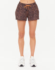 A person stands against a plain white background, wearing The Upside's LUDLOW BILLIE RUN SHORT in leopard print with an orange drawstring and white sneakers. The image is cropped from the waist down.