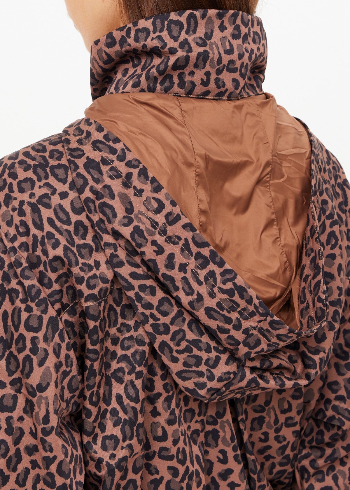 A close-up of a person wearing The Upside's LUDLOW ACE SHELL JACKET, a brown and black leopard print, water resistant jacket with a shiny brown hood lining, focused on the upper back and shoulder area.