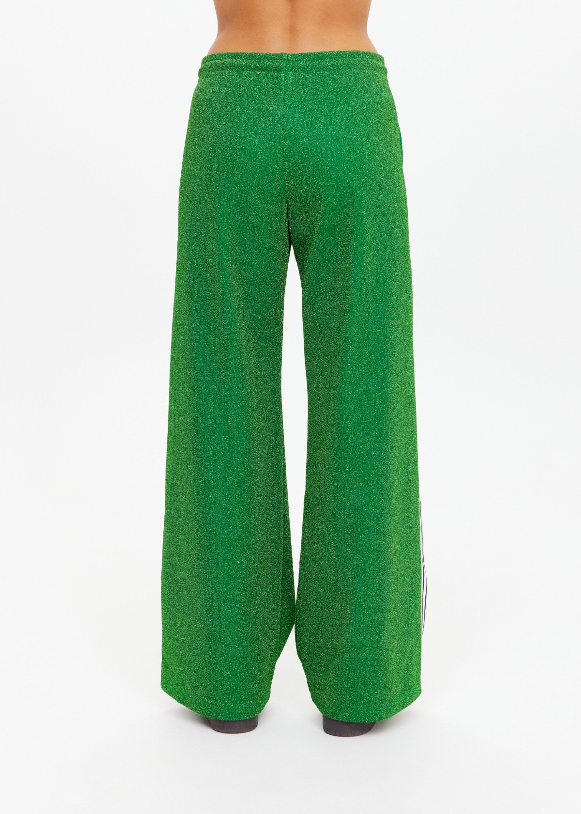 A person stands with their back to the camera in The Upside's GALAXIA LORETTA PANT, crafted from Amazon Green sparkle fabric, set against a plain white background.