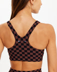 A woman with long brown hair wears The Upside TECHNICA JADE BRA and matching bottoms in a brown and black checkered print, shown from the back against a plain white background.