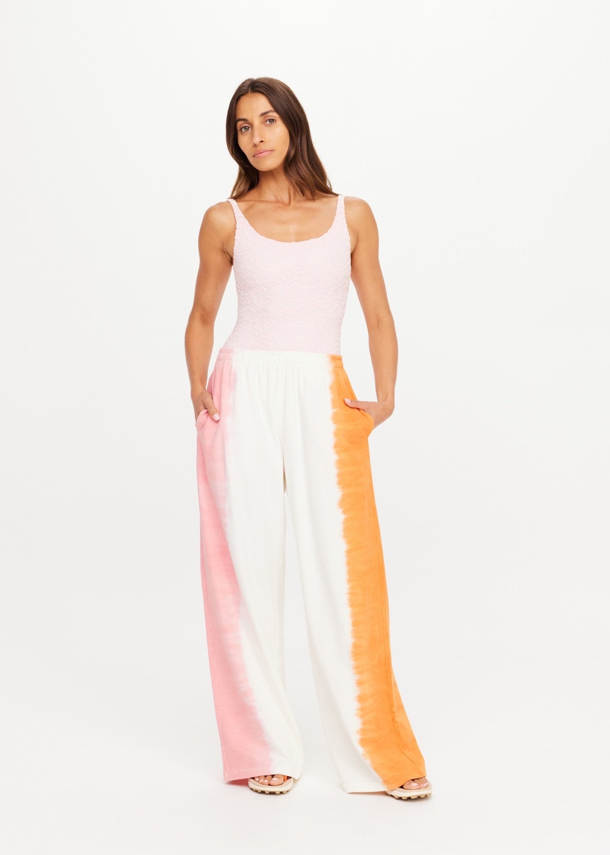 Pink-orange striped wide leg pants by The Upside, styled with a sleeveless pink top, hands in pockets.