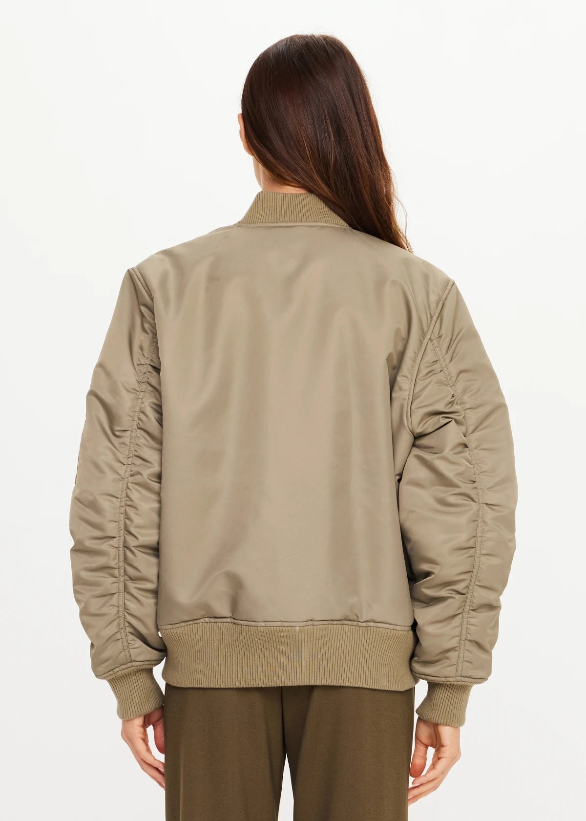The Upside Tribute Bomber Jacket in olive, shown from the back, styled with brown pants.