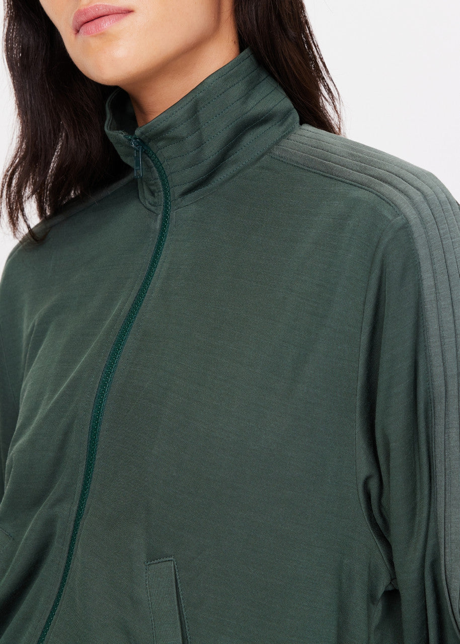 A person wearing The Upside&#39;s Roulette Lopez Jacket, a dark green zip-up with a high collar. The deep green fabric showcases a subtle striped pattern on the shoulder, and the face is partially out of the frame.