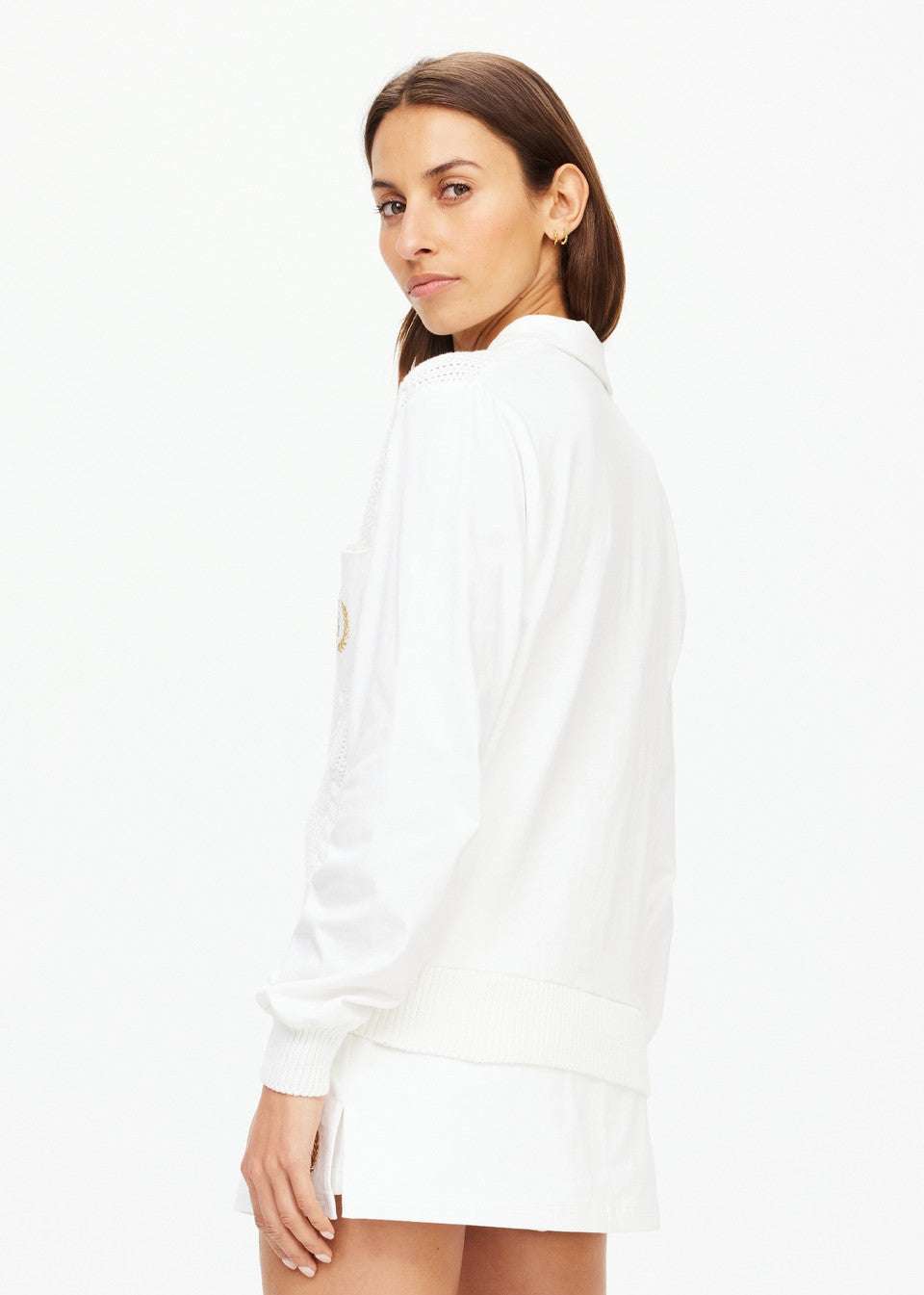 A woman with long brown hair is standing sideways, looking at the camera. She is wearing a Baccarat Violette Sweater by The Upside, and shorts crafted from organic cotton, set against a plain white background.