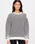 A woman with long dark hair wearing The Upside's Boo Knit Sweater, a classic style black and white organic cotton sweater, stands against a plain white background. She is facing forward, with her hands resting at her sides.