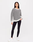 A person wearing The Upside's Boo Knit Sweater, paired with black leggings and white sneakers, stands against a plain white background. They have long dark hair and look directly at the camera with a relaxed posture.