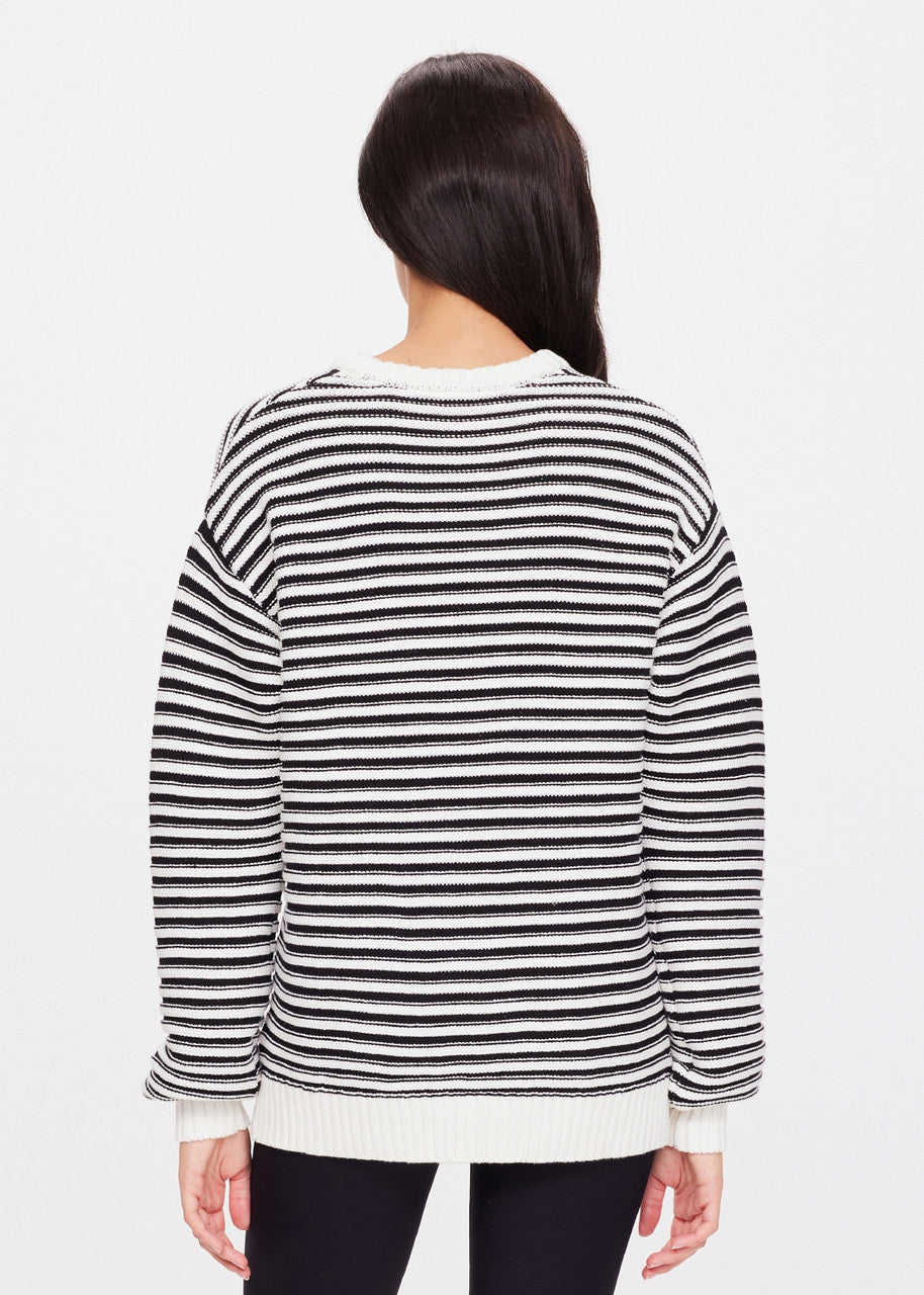 A person with long dark hair is wearing The Upside's Boo Knit Sweater, crafted from organic cotton, and standing with their back to the camera against a plain white background.