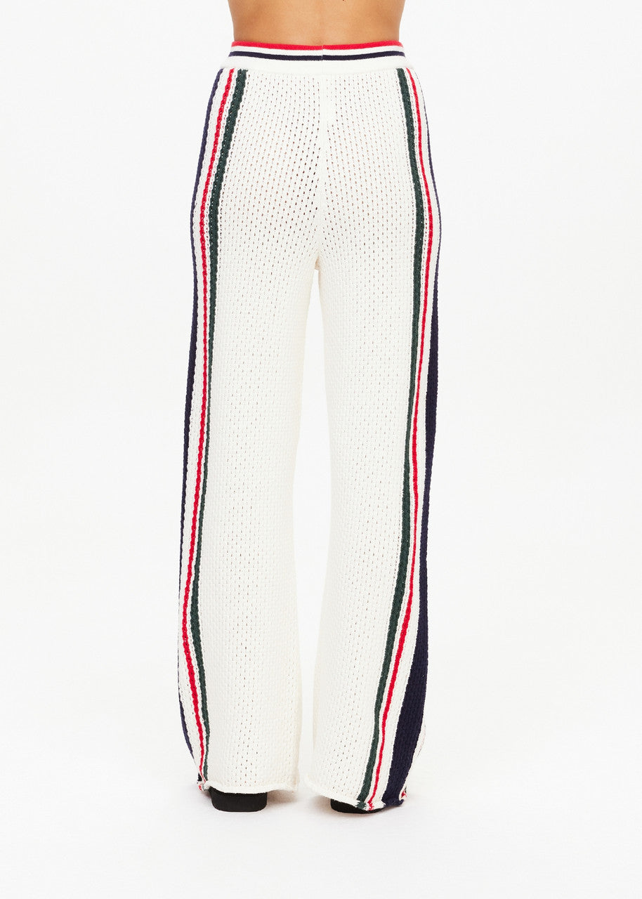 A person is dressed in the Reverie Kansas Pant by The Upside, featuring high-waisted, wide-leg pants crafted from striped knit fabric. These organic cotton trousers display vertical red, blue, and green stripes down the sides for a vibrant touch as they pose against a plain background.