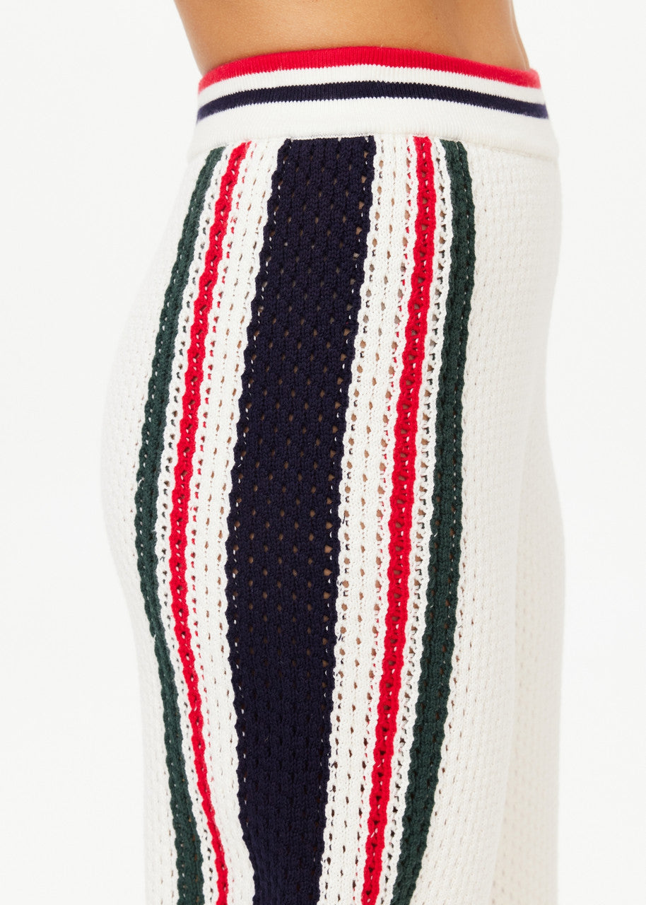 Close-up of a knitted garment in organic cotton, featuring vertical stripes in red, navy blue, and green on a white background. The fabric exhibits a textured pattern, with the waistband adorned with red and navy blue stripes. Perfectly paired with the Reverie Kansas Pant from The Upside for a casual yet stylish look.