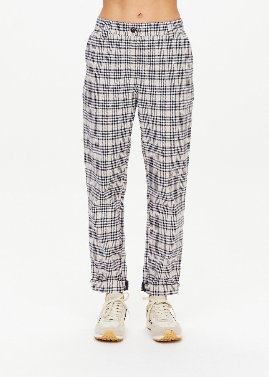 A person wearing The Upside's Highlands Pant, featuring a black and white checkered design, combined with white sneakers. Made from organic cotton, these pants provide comfort with their elastic waistband, set against a plain white background.