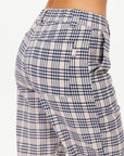 A close-up image showcases someone dressed in The Upside Highlands Pant, a beige and black plaid garment. These pants feature an elastic waist and a classic checkered pattern crafted from organic cotton. There is also a back pocket with a small label visible. The background is plain white.