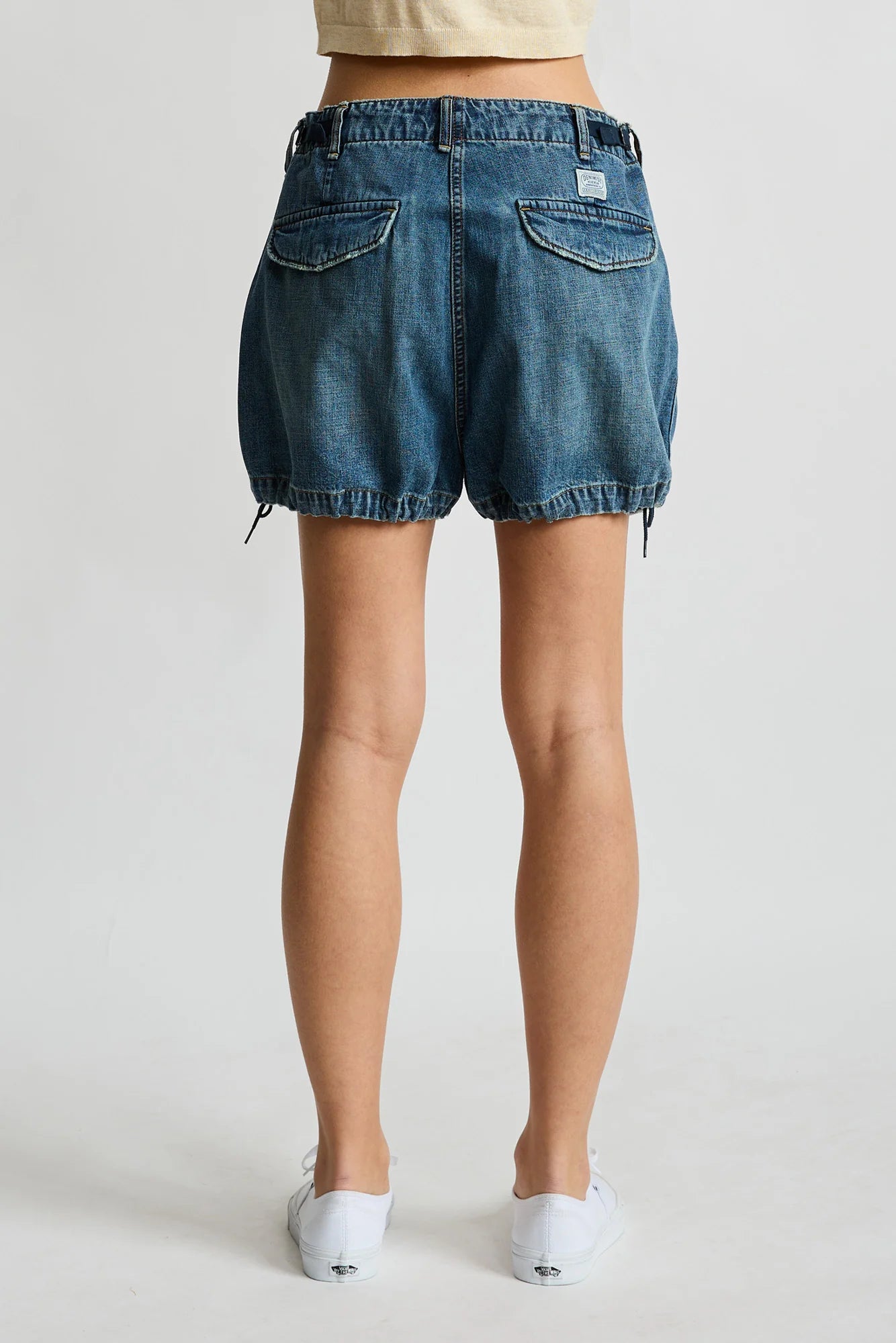 Denimist Utility Short in rigid indigo denim, shown from the back, paired with white shoes on a plain background.