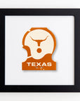 A framed artwork featuring a stylized silhouette of a longhorn's head in white acrylic on an orange background with "TEXAS" written below, all enclosed in a Match South Art Square Black Frame.