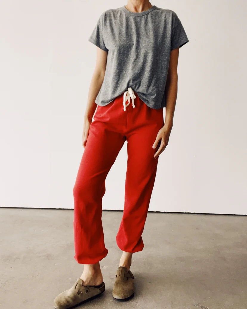 A person in a casual outfit featuring a gray French terry T-shirt and bright red "The Sweatpants" by Hey Gang, complemented by brown slip-on shoes, stands on a concrete floor against a plain white background.