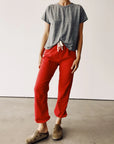 A person in a casual outfit featuring a gray French terry T-shirt and bright red "The Sweatpants" by Hey Gang, complemented by brown slip-on shoes, stands on a concrete floor against a plain white background.