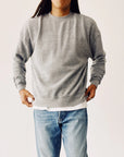 A person with long hair wears The Boxy Sweatshirt by Hey Gang, styled in an oversized vintage look, layered over a white shirt and blue jeans, standing in a neutral pose against a light background.