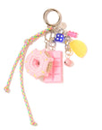 The Venessa Arizaga Bag Key Leash is a cute bag charm with playful food charms—a crocheted pink donut, pink chocolate bar—plus a blue die, yellow lemon slice, pink beads, bell, braided cord, all on a metal ring.