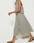 A person wearing the Nation LTD Vida Skirt, a black and white sleeveless striped dress with an elastic waistband, walks to the left in black sandals against a plain white wall.