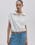 A woman stands against a plain background, confidently wearing the Rag & Bone vintage terry half zip muscle tee with a collar and drawstring hem, paired with blue drawstring denim jeans. Her hair is pulled back as she looks at the camera.