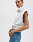 A person in a vintage look stands against a plain white background, wearing high-waisted blue jeans and the Rag & Bone vintage terry half zip muscle tee, gazing at the camera with a relaxed pose.