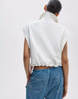 A person with their hair in a bun is seen from behind, wearing Rag & Bone's vintage terry half zip muscle top in white and blue jeans. A tattoo decorates their upper left arm.