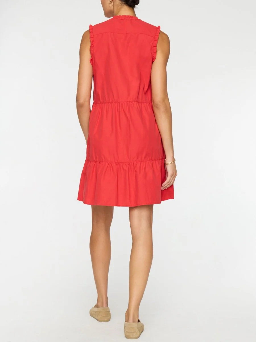 A person faces away from the camera wearing the VIOLA DRESS by BROCHU WALKER, a sleeveless, knee-length feminine dress with ruffle details, paired with beige flat shoes on a plain white background.