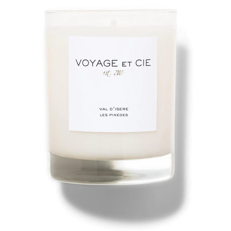 A 14 OZ Classic Highball soy coconut blend candle by Voyage Et Cie, in a clear jar labeled "VOYAGE ET CIE est. 2005" and "VAL D’ISERE LES PINEEDS," sits unlit, casting a soft shadow to the right.