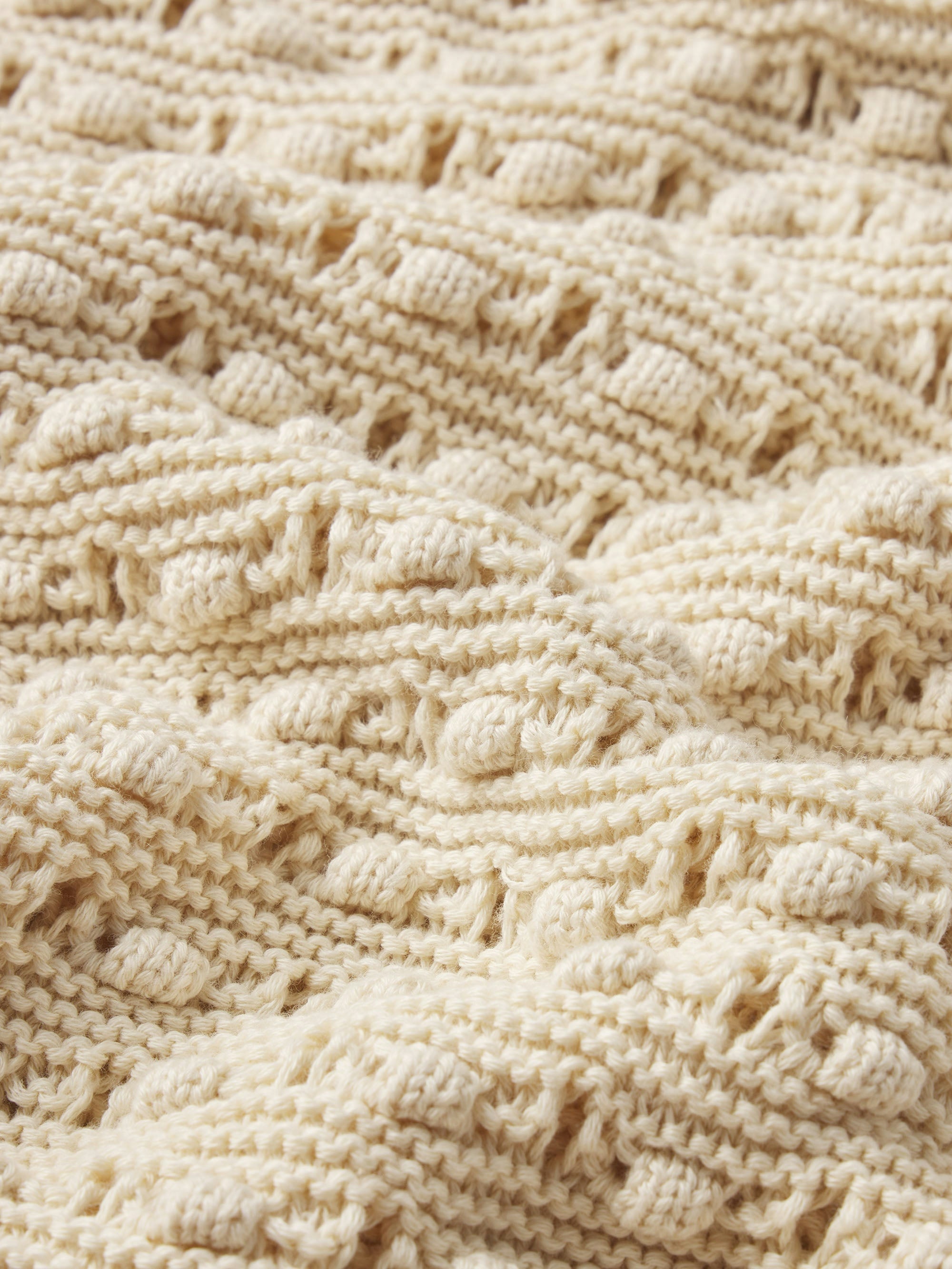 Close-up of The Bauble Skirt by FRAME, showcasing cream-colored knitted fabric with raised cables and bobbles for a cozy, textured, and intricately designed look.