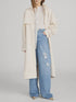 A woman wears FRAME’s The Field Trench over a white blouse and high-waisted, wide-leg distressed jeans, styled with beige pointed-toe shoes. Her face is partially out of frame.