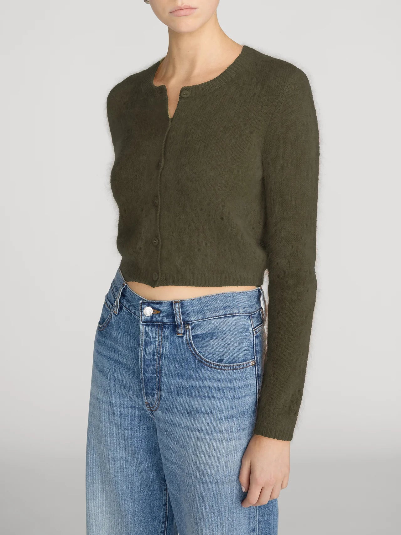 Olive green cropped cashmere cardigan by FRAME paired with blue jeans, styled against a neutral background.