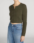 Olive green cropped cashmere cardigan by FRAME paired with blue jeans, styled against a neutral background.
