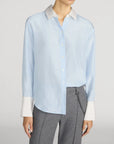 The Silk Standard Shirt by FRAME with contrast collar and cuffs, styled with gray pants in a modern setting.