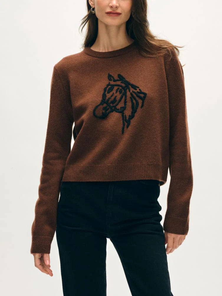 A woman wears the White + Warren Horse Embroidered Crew, a brown Western sweater featuring a hand-embroidered black horse's head on the front, paired with black pants against a plain light background.