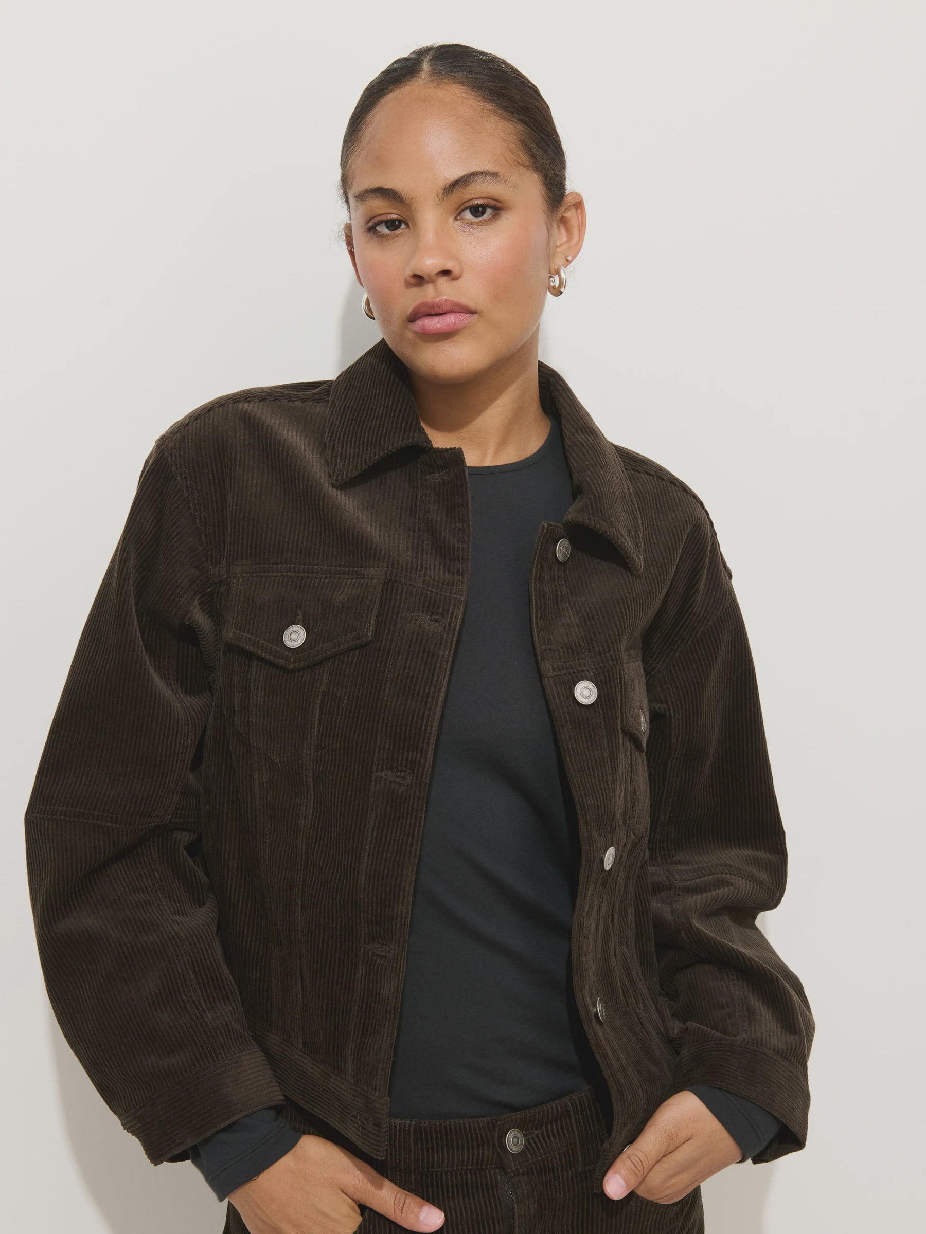A person with pulled-back hair wears the Alex Mill Camden Rider Jacket in corduroy over a black top, standing against a plain white background with a neutral expression.