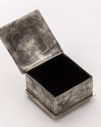 The J Alexander Rustic Silver Small Stamped Box w/ Turquoise features ornate silver detailing and a black interior, adding a Southwestern touch to any space as it sits elegantly on a light surface.