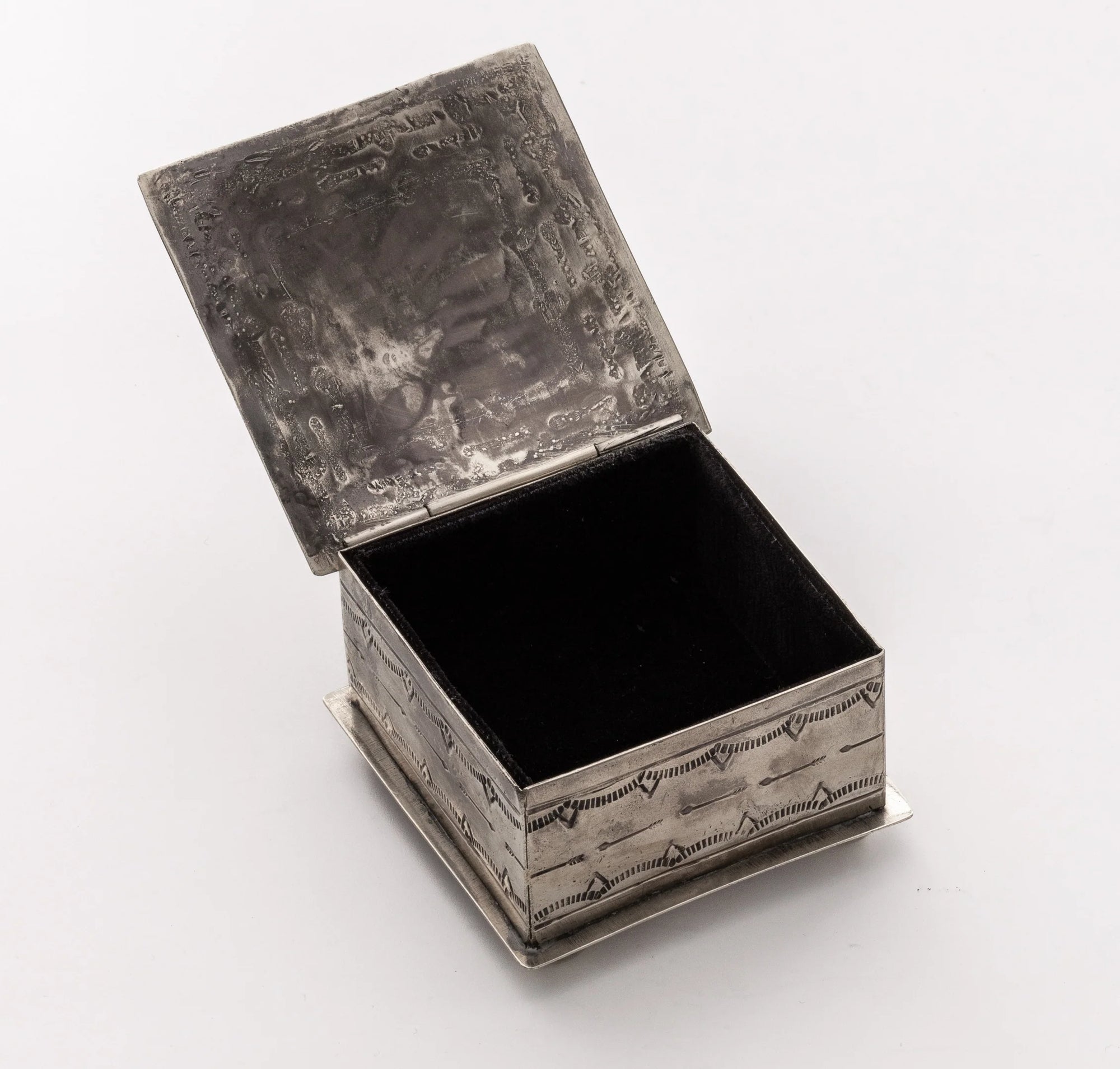 The Small Stamped Box w/ Turquoise Cross by J Alexander Rustic Silver features a square silver metal design with an intricate pattern, hinged lid, and a rich dark interior—ideal for keepsakes and Southwestern decor.