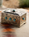 The J Alexander Rustic Silver 9 Stone Turq Box features engraved patterns and turquoise stones, displayed on a geometric woven fabric in brown, orange, and cream—perfect for adding a Southwestern touch to your space.