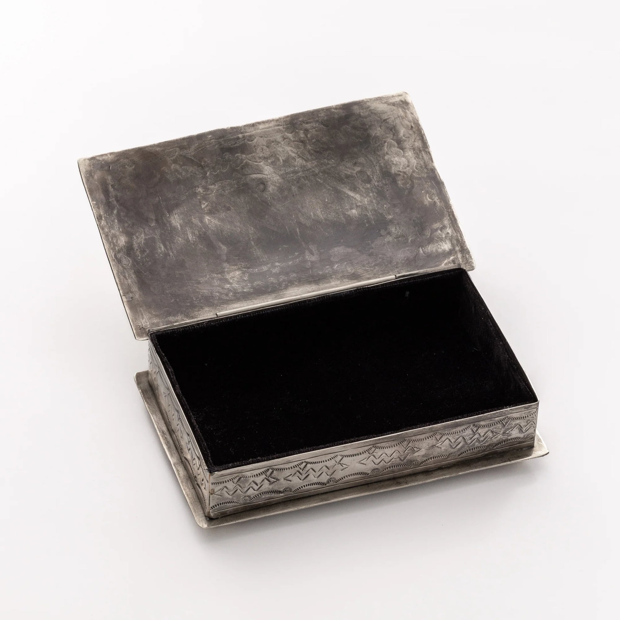 The Stamped Rec Box Turq by J Alexander Rustic Silver features a rustic, rectangular design with an open hinged lid and engraved patterns, making it a charming Southwestern accent. Displayed on a plain white surface, the box reveals a dark, empty interior.