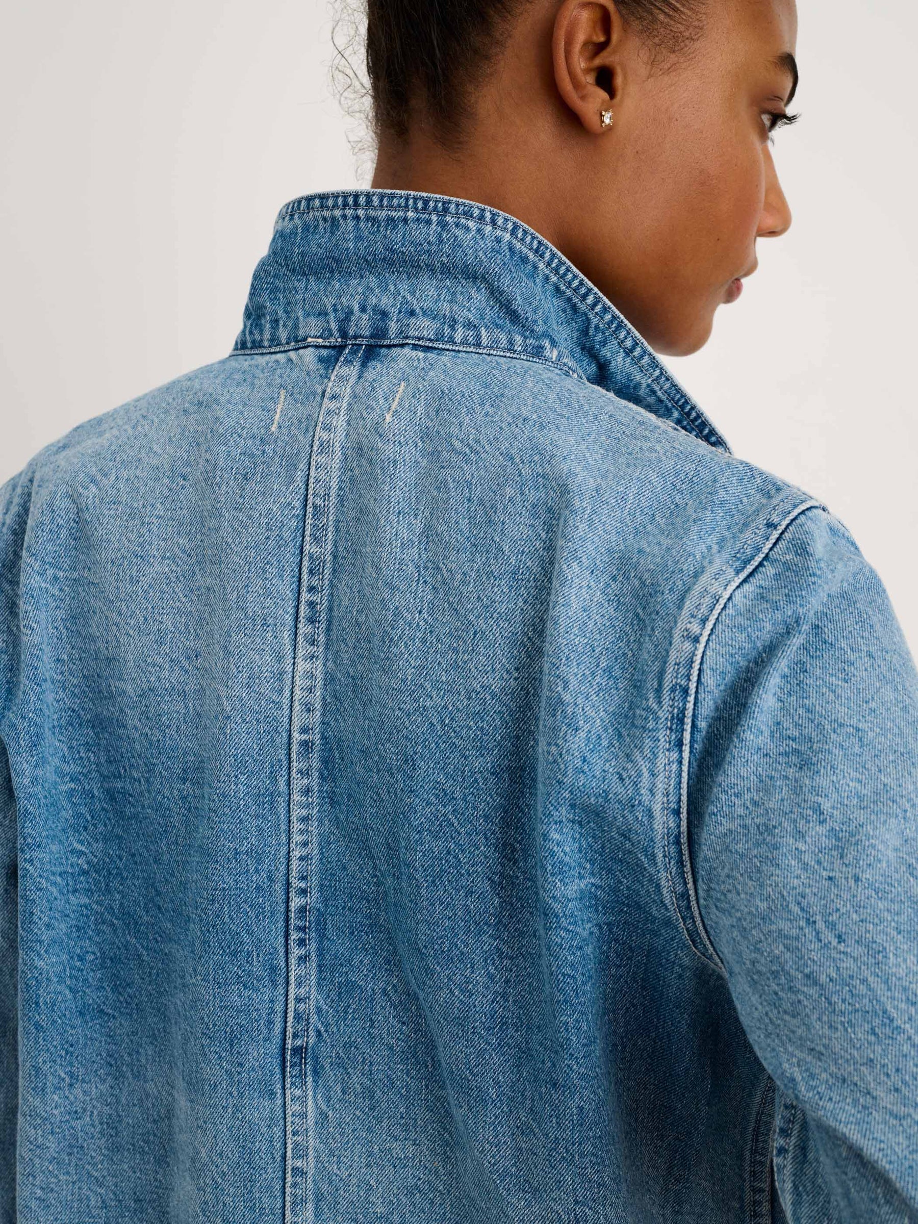 A person with short hair is seen from behind wearing the Alex Mill Britt Work Jacket, a garment-dyed denim piece with the collar turned up, against a plain light-colored background.