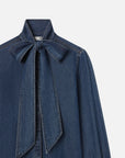 The FRAME Secretary Blouse is a stylish denim shirt with long sleeves and a bold bow at the collar, providing a contemporary update to the traditional design.