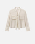 The FRAME Polka Dot Modern Tie Blouse is a cream-colored, long-sleeve top with a tie-front neckline, two chest pockets, and a textured mesh-like pattern, shown on a plain white background.