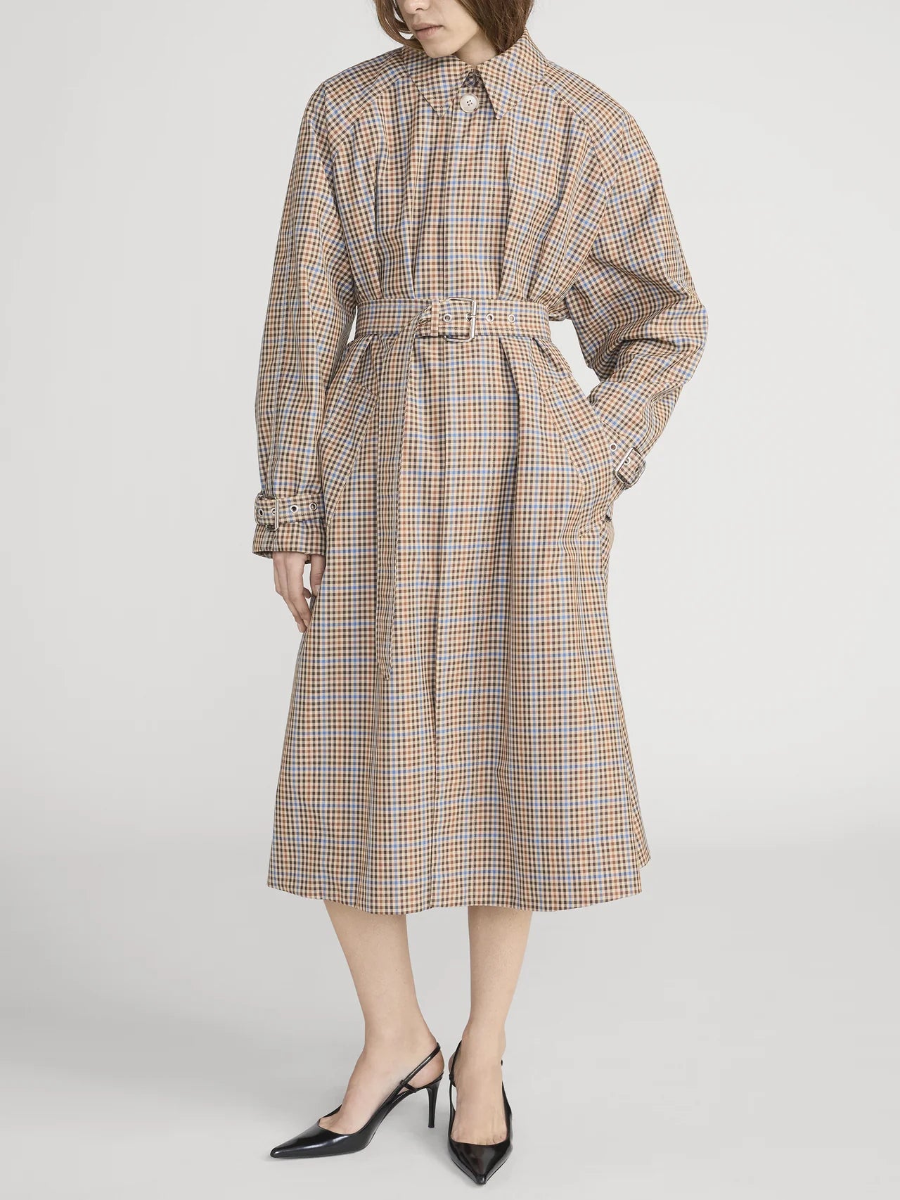 A person models the FRAME Plaid Mac Coat—a structured, tailored cotton-blend coat with a belted waist, long sleeves, and below-knee length—styled with black pointed-toe heels against a white background.