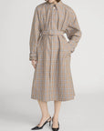 A person models the FRAME Plaid Mac Coat—a structured, tailored cotton-blend coat with a belted waist, long sleeves, and below-knee length—styled with black pointed-toe heels against a white background.