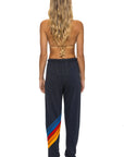 A woman with long wavy hair stands barefoot, wearing Aviator Nation’s all seasons circle chevron women’s sweatpant featuring colorful diagonal stripes and a vintage feel, hand sewn in Los Angeles.